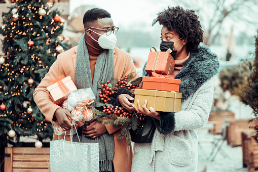 Young couple at Christmas shopping, COVID-19 pandemic. They wearing a protective mask to protect from corona virus COVID-19 and holding gift boxes